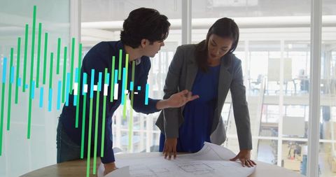 Young professionals collaborating over architectural blueprint in modern glass office atrium