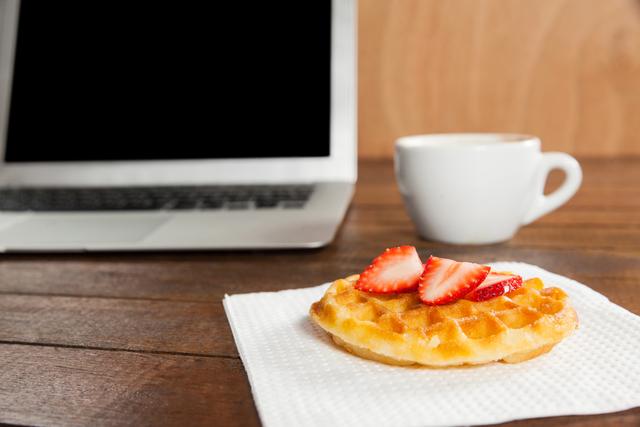 Office desk with strawberry waffle, laptop and coffee cup in office