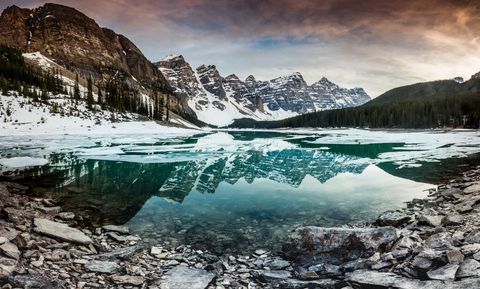 Turquoise glacier lake reflecting snowcapped mountain peaks at sunrise with rocky shoreline