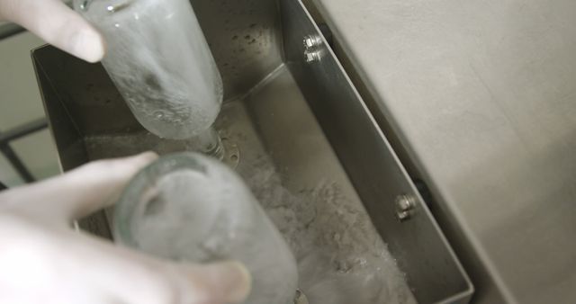 Technician wearing gloves sterilizing glass bottles with dry ice in a laboratory. Highly sterilized and safe process ensuring bottles are impeccably clean. Ideal for illustrating scientific research, laboratory procedures, cleanliness standards, safety protocols, and sterile environments.