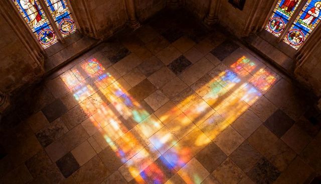 Stained-glass reflections casting warm prism color across checkered cathedral floor