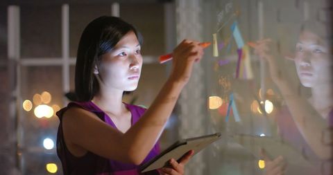 Businesswoman brainstorming with tablet on glass wall
