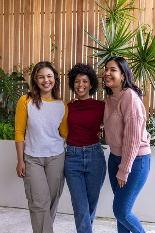 Diverse women smiling and embracing on sunlit courtyard patio with lush plants