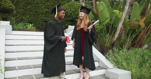 Young graduates celebrating on campus steps wearing mortarboards and gowns holding diplomas