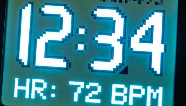 Closeup pixelated digital clock display showing 12:34 and hr 72 bpm with neon cyan backlight