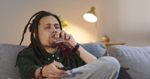 Man relaxing on couch drinking bottle beverage while holding remote and watching tv