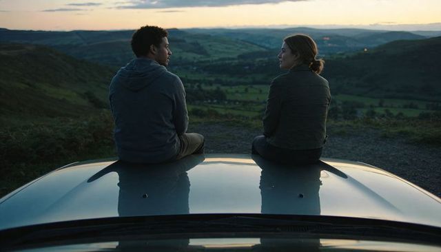 Couple sitting on car roof at dusk overlooking rolling valley sunset
