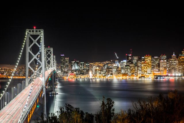 San Francisco Bay Bridge illuminated at night with the city's skyline in the background. Perfect for tourism campaigns, travel brochures, cityscape posters, and California travel guides.