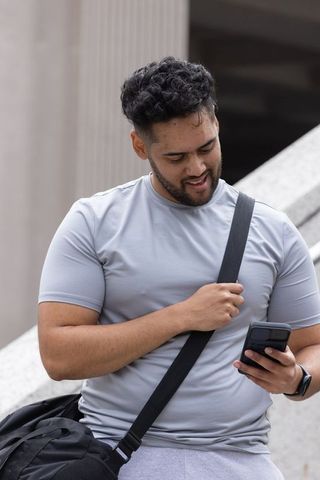 African american man checking smartphone while holding backpack strap on urban steps