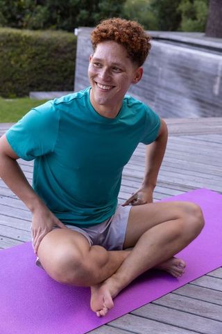 Man Twisting on Yoga Mat Outdoors with Relaxed Smile