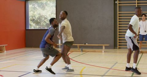 Coach directing african american men practicing basketball defense in indoor gym