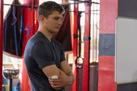 Focused young athlete standing with arms crossed by red rig in industrial gym