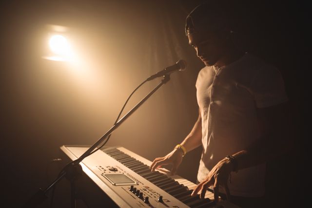 Male singer confidently playing piano on stage in a dimly lit nightclub. Ideal for use in articles about live music performances, nightlife entertainment, or promoting music events. Can also be used in advertisements for music venues or artist promotions.