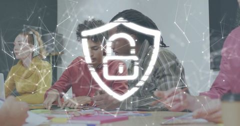 Multicultural team collaborating on tabletop brainstorming with cybersecurity shield overlay