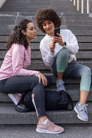 Women sharing workout app and fitness tips on smartphone while resting on urban steps