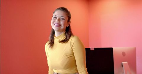 Smiling mid-adult woman standing in mustard turtleneck against coral pink office wall