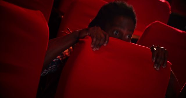 A person is peeking over the top of a red cinema seat, with copy space - Download Free Stock Photos Pikwizard.com