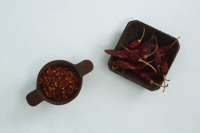 Dried red chili peppers and crushed red pepper in bowls on white background. Ideal for use in culinary blogs, recipe websites, cooking magazines, and food packaging designs to highlight spicy ingredients and seasoning options.