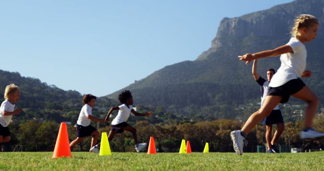 Children enjoying an outdoor race running through colorful cones on a field. Featuring a mountainous background and an instructor, this energetic scene highlights physical activity, teamwork, and outdoor fun. Suitable for illustrating sports activities, exercise programs, school events, teamwork, and fitness promotions.