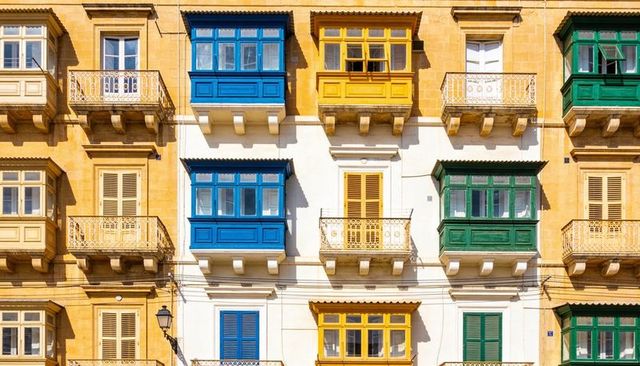 Sunlit maltese balconies in blue yellow green on warm limestone facade