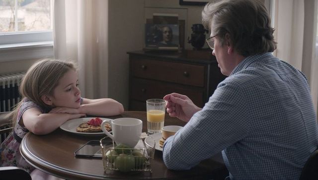 Father and daughter quiet morning breakfast, daughter watching while father eats pancakes