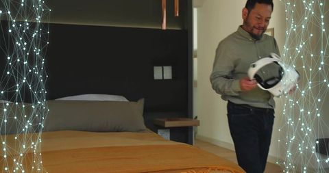 Mature asian man examining vr headset in minimalist contemporary bedroom for home tech use