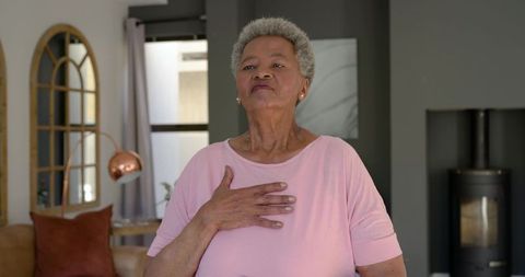Senior woman holding hand to heart practicing gratitude in cozy modern living room
