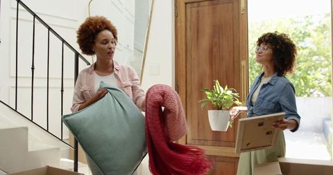 Diverse friends unpacking and decorating bright foyer with pillows, blanket, and plant