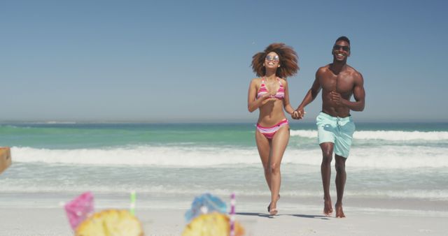 Happy diverse couple holding hands walking on sunny beach. Summer, vacation, romance, relaxation, happy time.