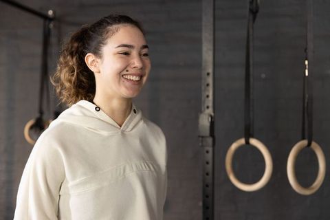 Smiling woman standing in gym with wooden rings, strength training and functional fitness