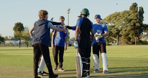 Youth cricket team exchanging handshakes and fist bumps on grass pitch at golden hour unity