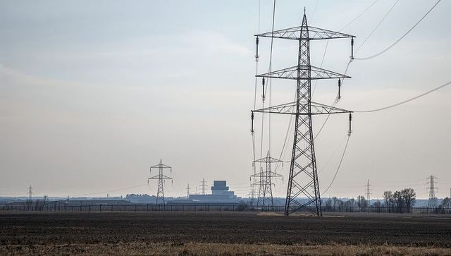Towering High-Voltage Transmission Towers Crossing Wide Fallow Field Under Overcast Sky