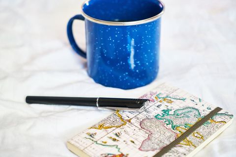 Blue enamel mug featuring world map notebook and pen for travel planning