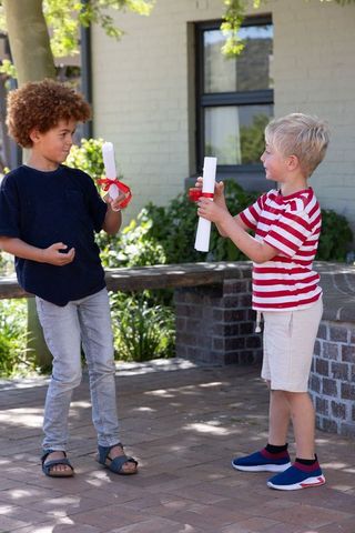 Diverse boys exchanging rolled diplomas outdoors celebrating friendship and achievement