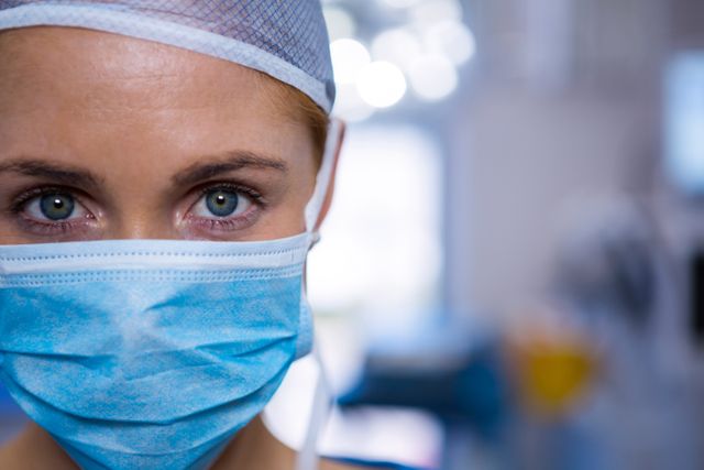 This image shows a female surgeon wearing a surgical mask and cap in an operation theater. Her eyes are focused, indicating concentration and professionalism. This image can be used for healthcare-related content, medical articles, hospital brochures, or educational materials about surgery and medical professions.