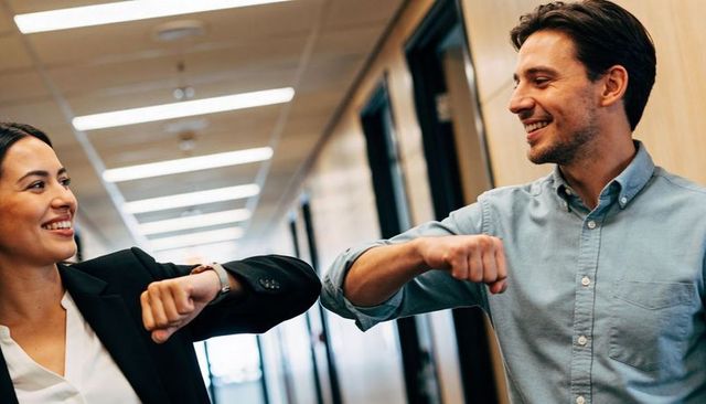 Colleagues exchanging elbow bump in office corridor smiling casual contactless greeting