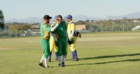 Baseball teammates exchanging high five on sunlit field while opponents stand holding gloves
