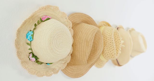 A collection of various straw hats is displayed on a white wall, with copy space. Each hat features a unique design, suggesting a personal touch or a reflection of different styles and preferences.