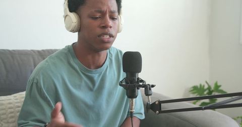 African american podcaster recording at home wearing headphones and speaking into microphone