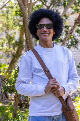 Young african american man smiling in sunny garden wearing white shirt and brown satchel