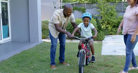 Father teaching son to ride bicycle in family backyard interaction
