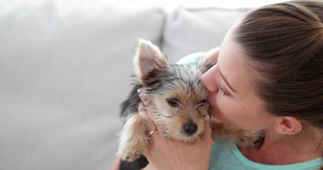 This image shows a woman kissing and holding a cute Yorkshire Terrier puppy. It is great for use in pet care advertisements, animal rescue campaigns, and promotional materials for dog training or pet education services. Also suitable for illustrating articles about the benefits of pet ownership and the human-animal bond.