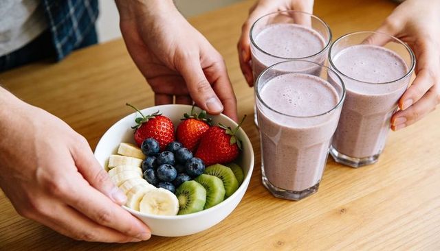 Serving fresh fruit bowl with strawberry banana smoothies on wooden breakfast table