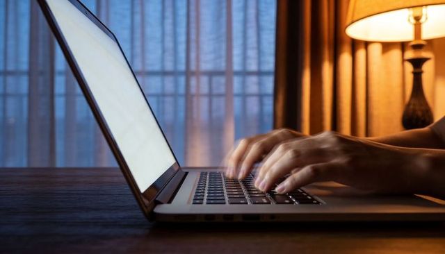 Typing hands on laptop at dusk with warm lamp glow for remote work and focus