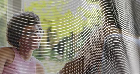 Smiling woman wearing glasses chatting through ripple glass panel at bright lounge window