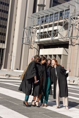 Diverse female graduates celebrating on urban campus plaza holding diplomas