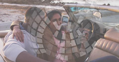 Couple embracing in convertible on coastal road holding smartphone enjoying seaside sunset