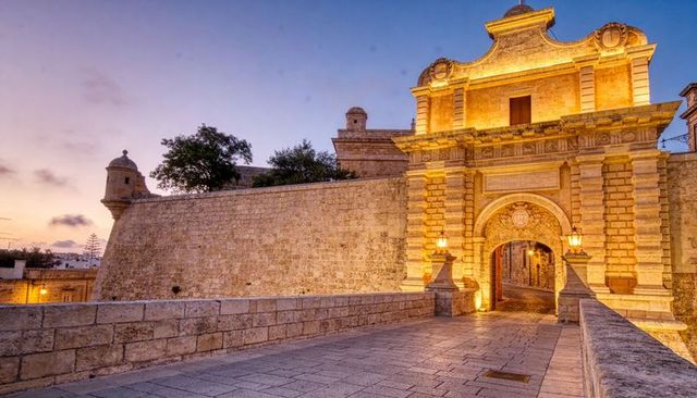 Golden-lit stone gateway and causeway at dusk, historic fortress archway with turret
