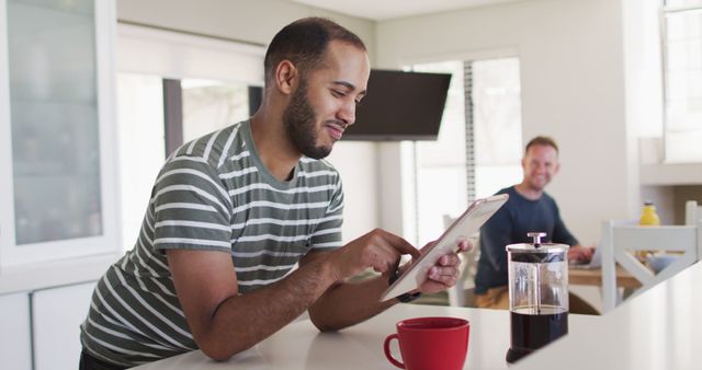 Young Man Enjoying Morning Coffee while Browsing Tablet in Modern Kitchen - Download Free Stock Images Pikwizard.com