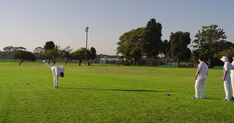Cricket bowler delivering final stride while teammates watching on green practice field